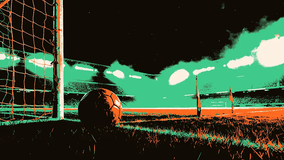 Un ballon de football usé posé sur l'herbe devant un filet ouvert, avec des drapeaux de corner encadrant les cages et des gradins vides dans la brume, illustrant la fin d'un match de coupe africaine.