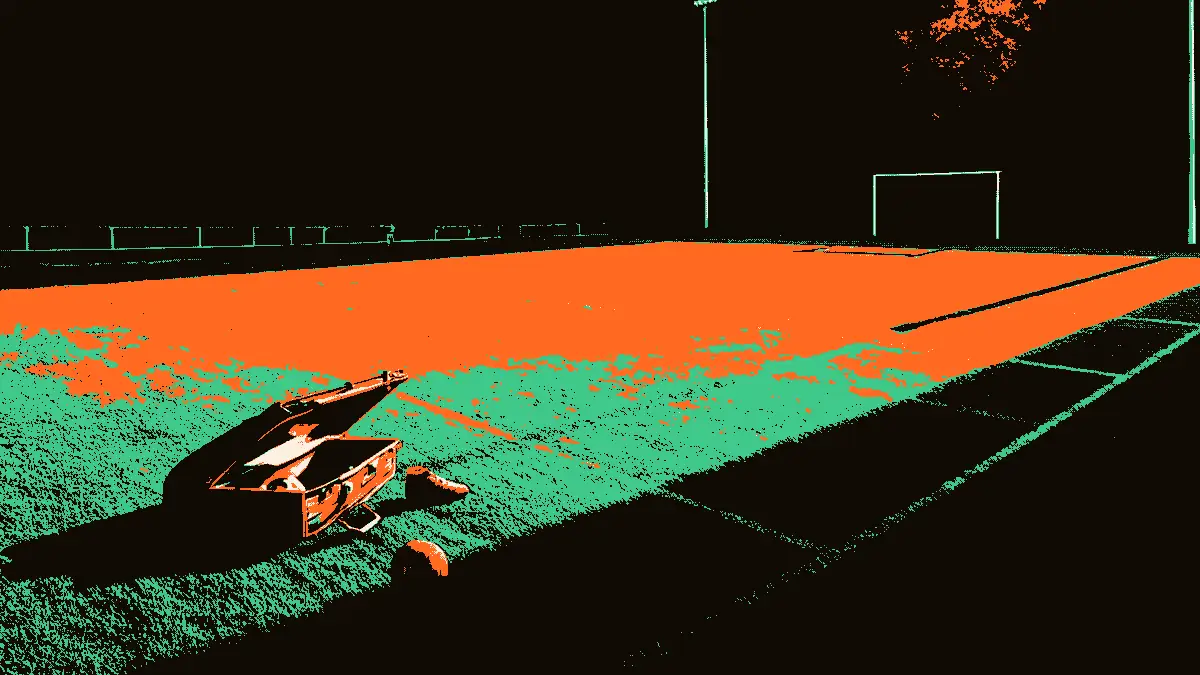 Vue d'un terrain de football vide avec, au premier plan, une valise ouverte posée sur l'herbe à côté d'un crampon isolé et d'un ballon, sous la lumière crue de projecteurs, évoquant un départ imminent.