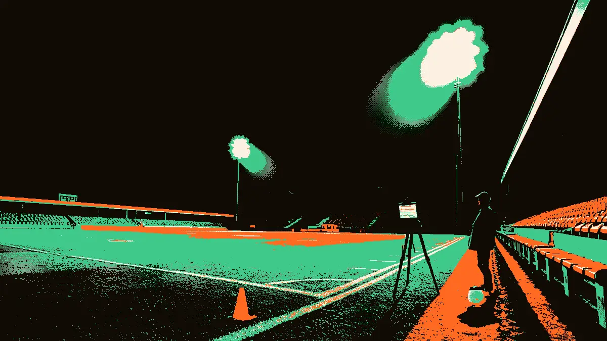 Un terrain de football vide sous des projecteurs allumés en soirée, avec un banc de touche désert au premier plan et un ballon, un sifflet et une planchette tactique posés sur un trépied, évoquant une feuille de match en cours de composition.